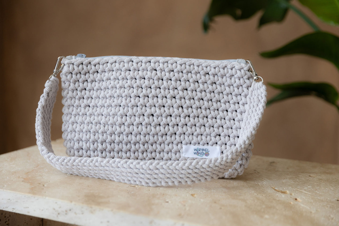 Nahaufnahme des vorangegangenen Bildes. Die Tasche und der Tisch sind scharf, der Hintergrund ist unscharf. Wir sehen deutlich das Muster und das Garn der Tasche. Der Schultergurt hängt vorne über die Tasche.