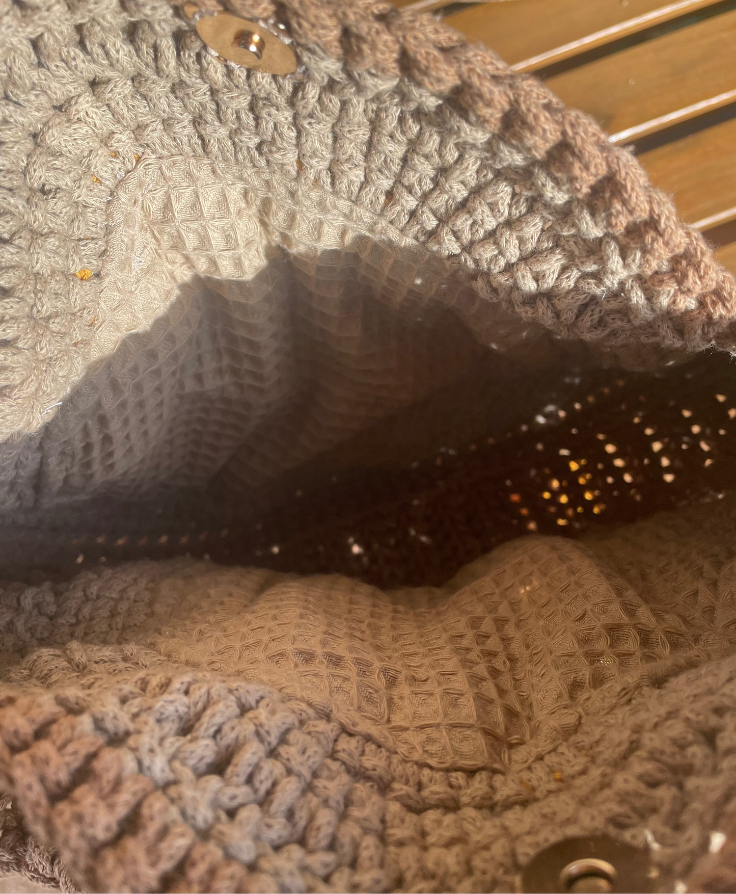 Nahaufnahme des Innenraums. Hinter den Sonnenblumen befindet sich ein Innenfutter im selben Sandbraunen Ton, wie das Garn. Außerdem sehen wir den goldenen Magnetknopf, mit dem die Tasche verschließbar ist.