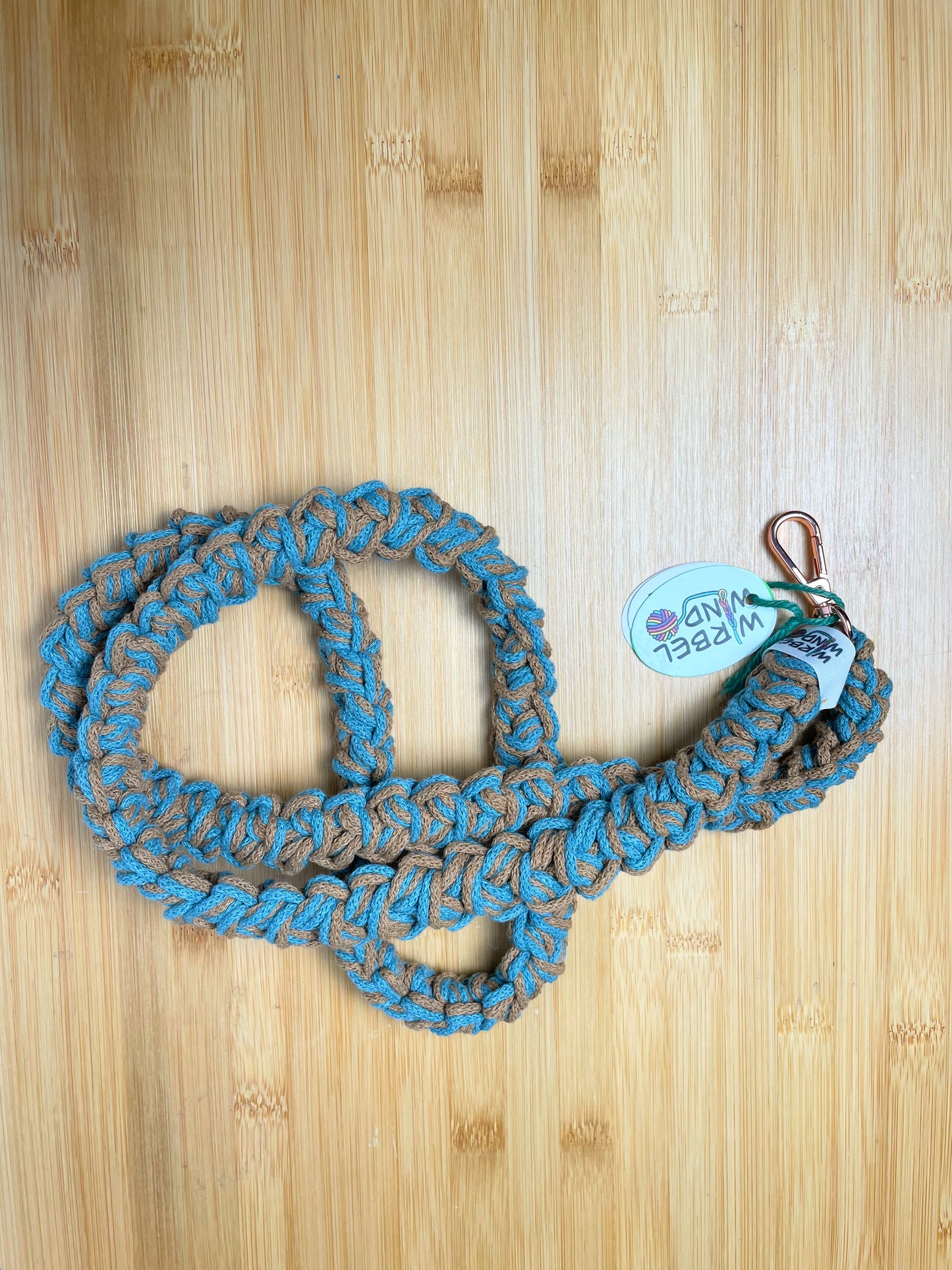 Karamellbraun-Trkisblau-meliertes Lanyard kringelt sich. Wirbelwindlogo am unteren Ende, direkt über roségoldenem Karabiner angenäht.