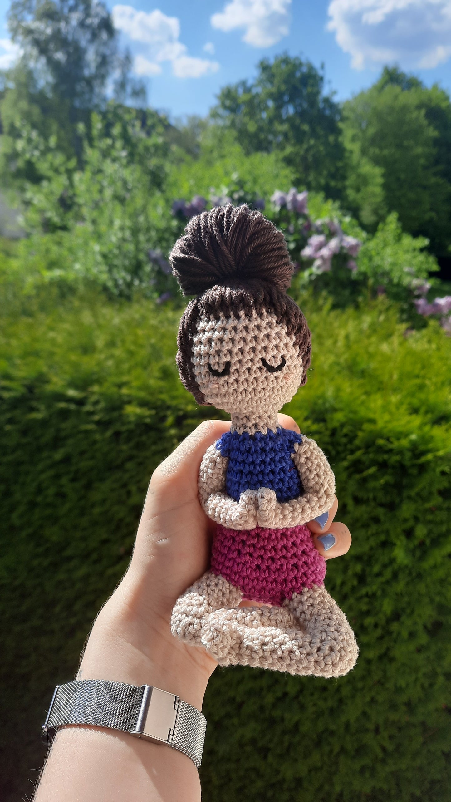 Weibliche Puppe Hände vor dem Herzen zusammen, im Schneidersitz, Augen geschlossen, rosa Wangen, dunkelbrauner großer Dutt, dunkelblaues aärmelloses Shirt, pinke Shorts, heller Hautton.