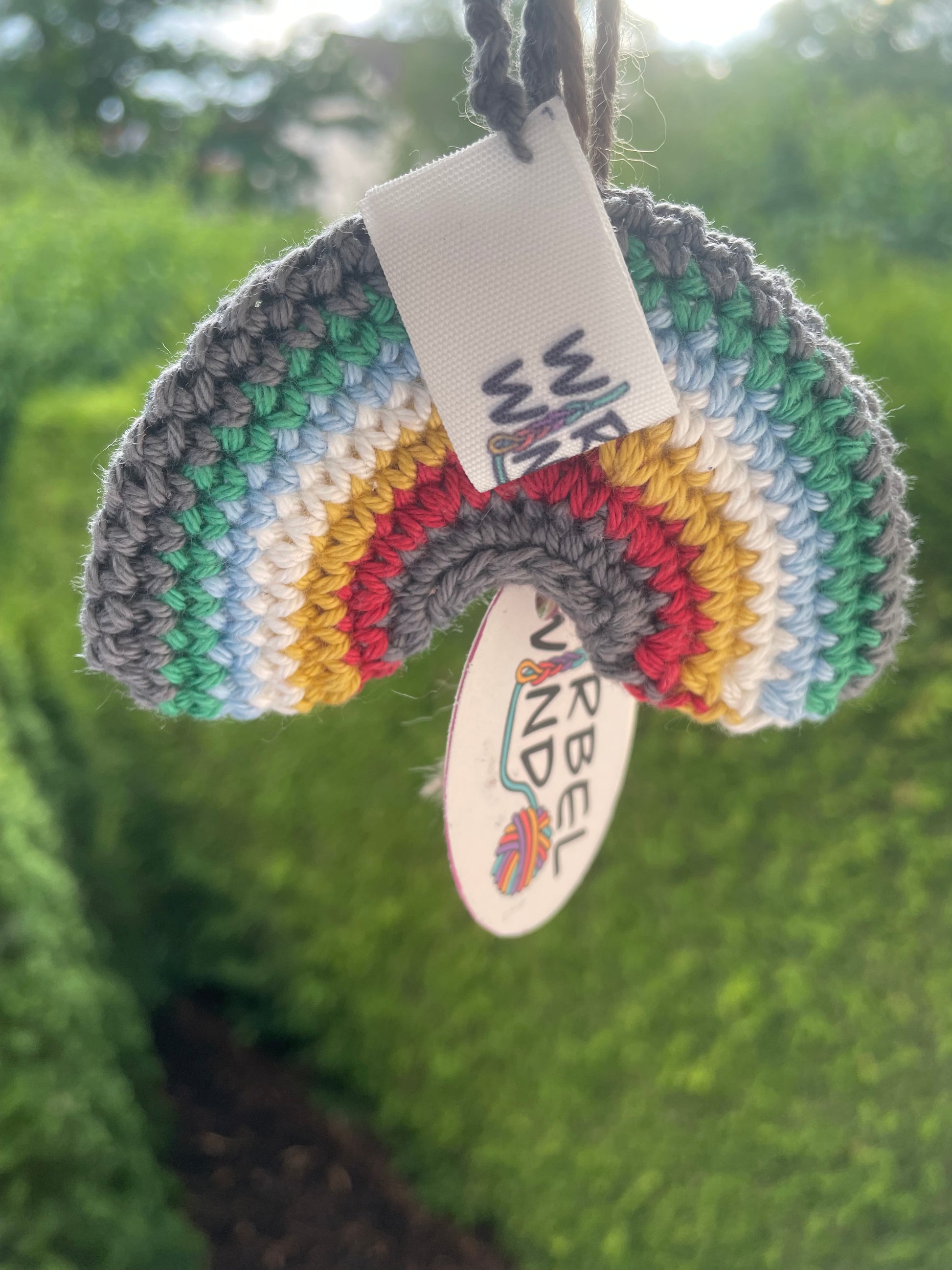 Gehäkelter Regenbogen Schlüsselanhänger mit Karabiner in den 6 Farben der Disability Pride Flagge: Grau, Grün, Blau, Weiß, Gelb, Rot. Das Logo von Wirbelwind hängt vorne.