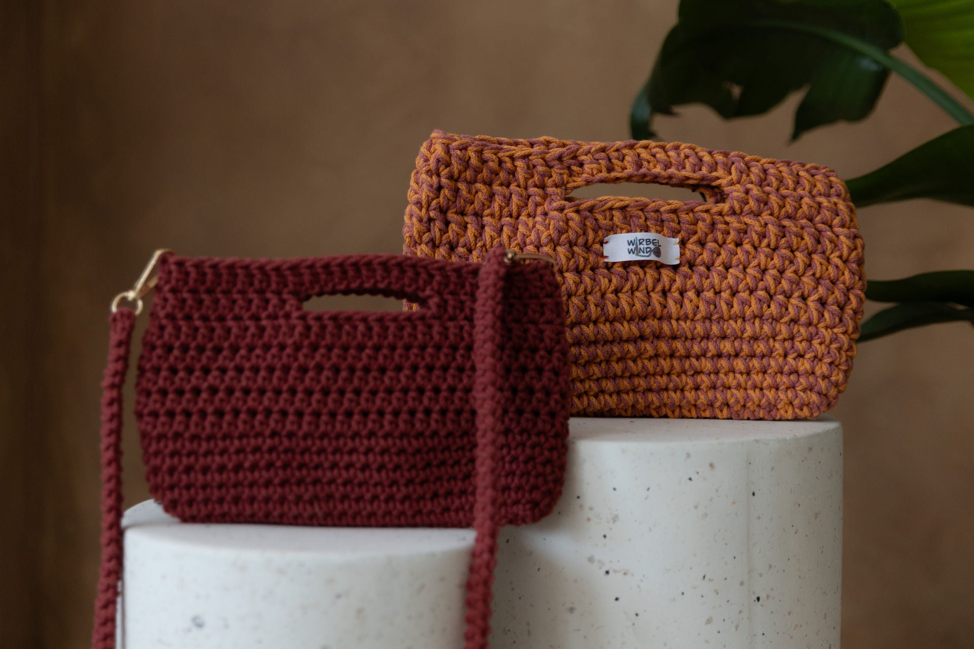 Nahaufnahme der Molly Medium Tasche in Pink & Orange und der Molly Mini Tasche in Weinrot, wie sie auf den Bettonsäulen stehen. Sie füllen fast den ganzen Bildschirm aus. Die kleine Tasche im Vordergrund ist unscharf, der Fokus liegt aus der hinteren.
