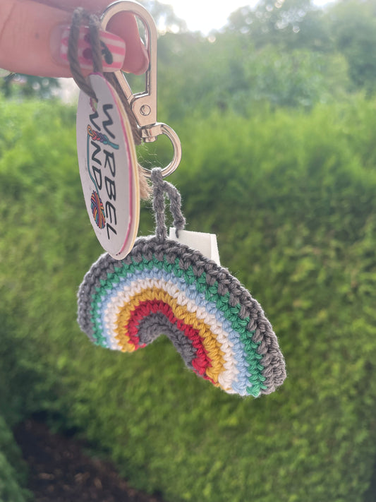 Gehäkelter Regenbogen Schlüsselanhänger mit Karabiner in den 6 Farben der Disability Pride Flagge: Grau, Grün, Blau, Weiß, Gelb, Rot. Außerdem hängt das Logo von Wirbelwind ebenfalls am Karabiner.