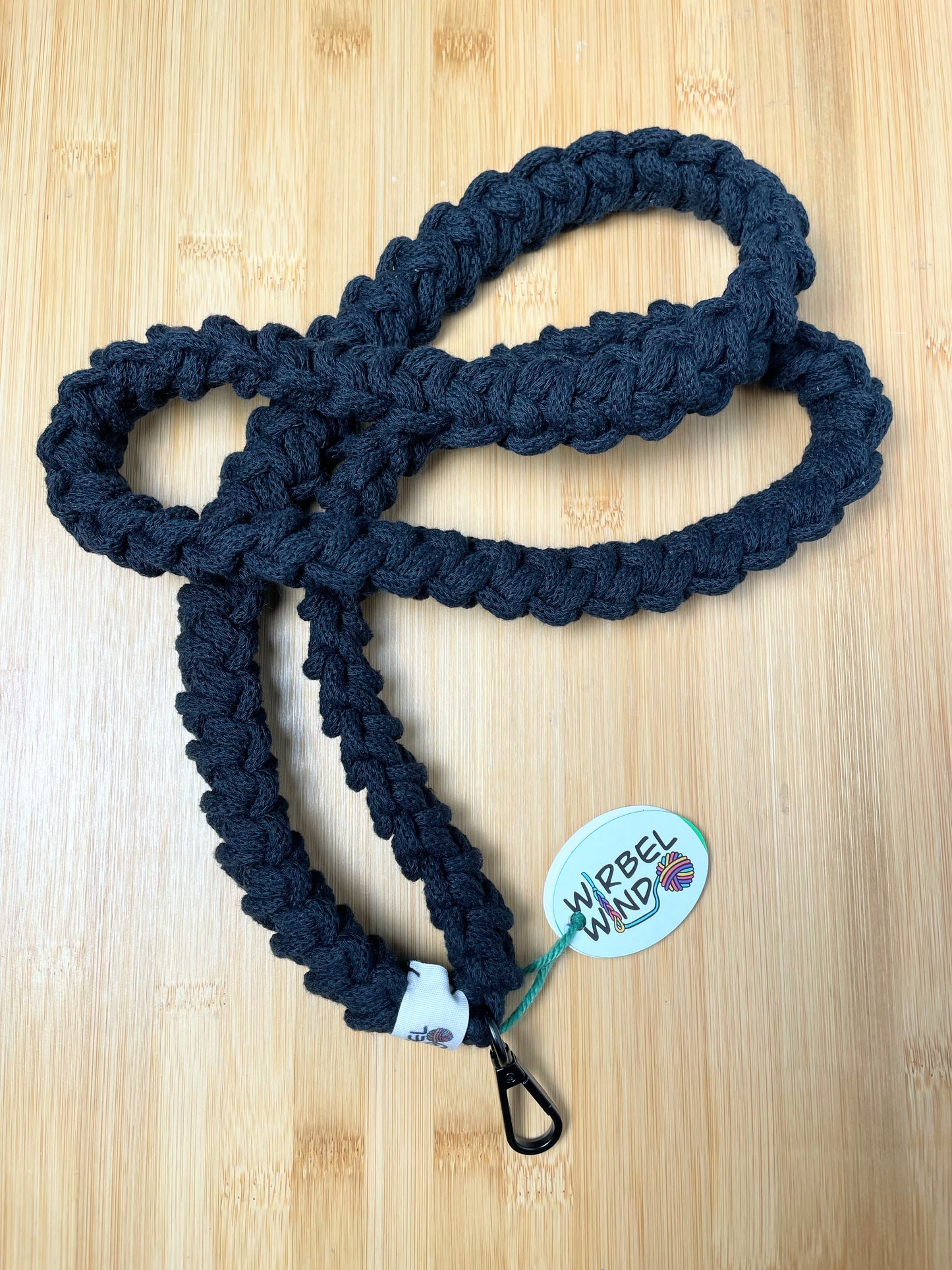 Schwarzes Lanyard kringelt sich. Wirbelwindlogo am unteren Ende, direkt über schwarzem Karabiner angenäht.