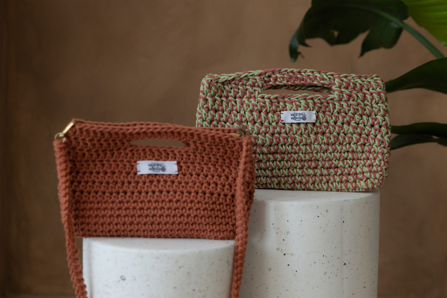 Nahaufnahme der Molly Medium Tasche in Pink & Hellgrün und der Molly Mini Tasche in Orange, wie sie auf den Bettonsäulen stehen. Sie füllen fast den ganzen Bildschirm aus. Die kleine Tasche im Vordergrund ist unscharf, der Fokus liegt aus der hinteren.