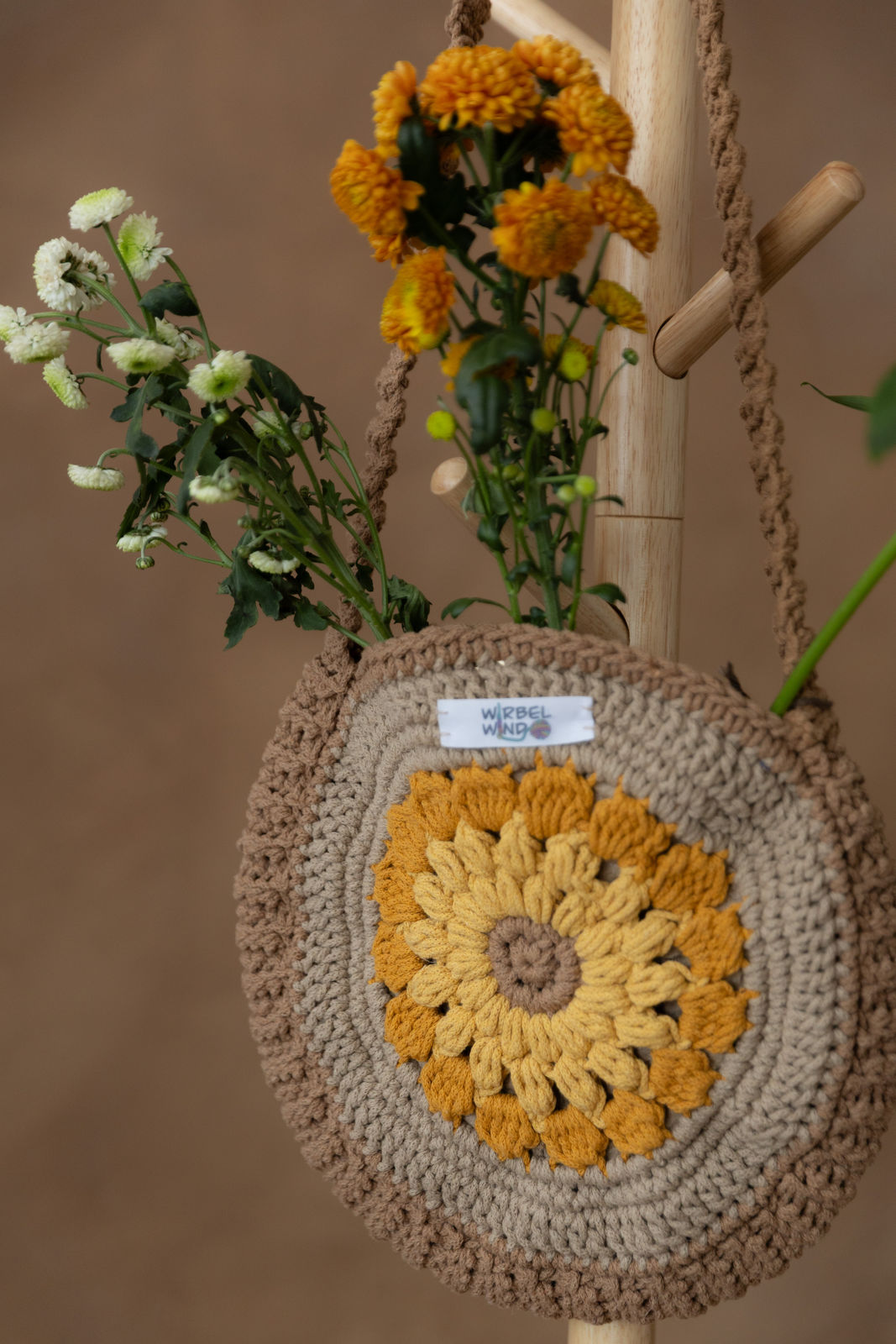 Nahaufnahme des vorherigen Bildes. Die gelben Blumen ragen rechts komplett aus dem Bild heraus. Die mittleren orangenen Blumen sind unscharf. Die weißen Blumen links sind scharf zu sehen. Das komplette muster der Sonnenblume und dem umrahmenden Kreis ist gut zu sehen. Das Logo das sich oben in der MItte befindet ist wieder etwas unscharf.