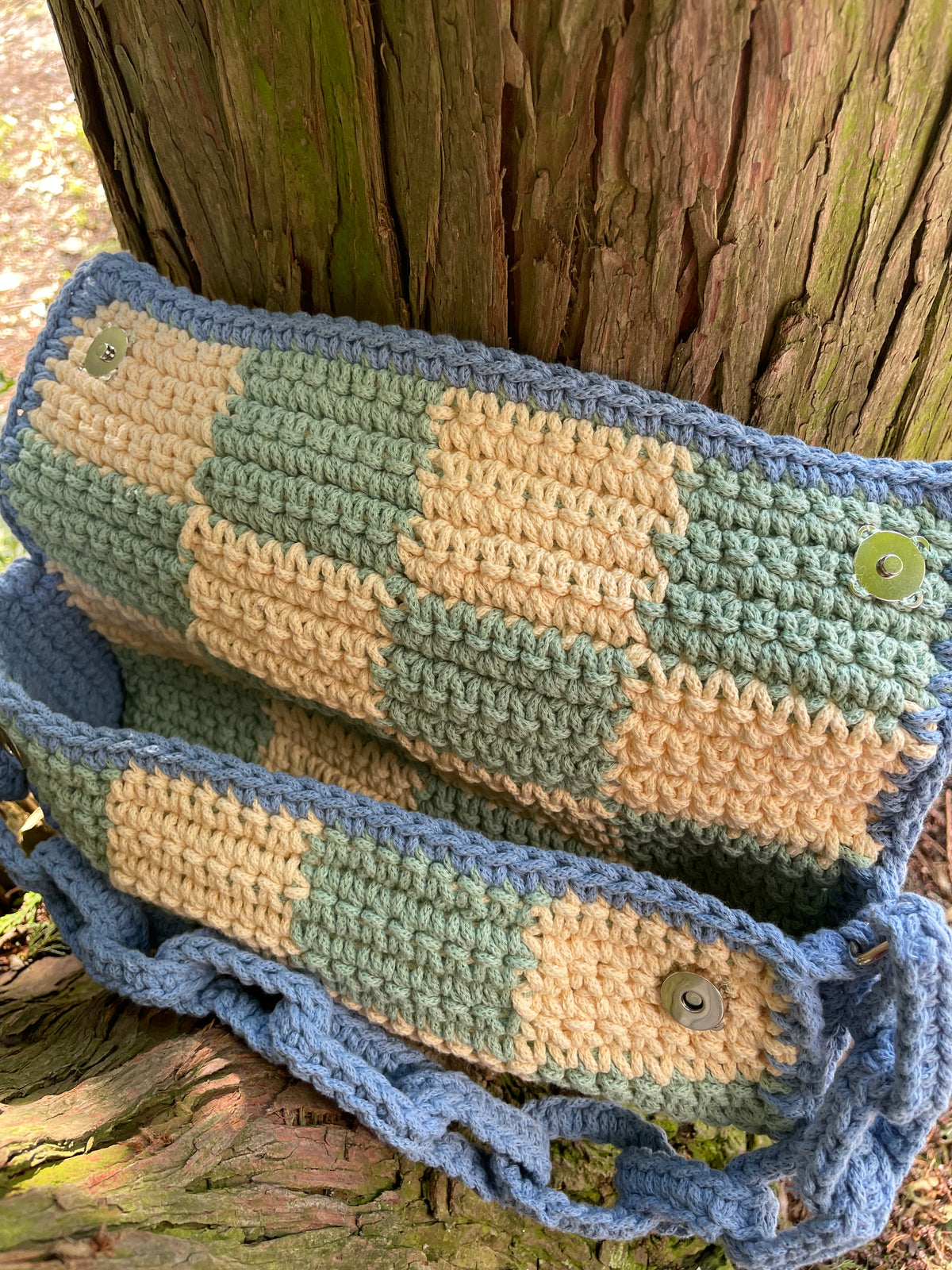 Blick von oben in die geöffnete Tasche: Links und rechts 1 Magnetknopf, Boden gerundet, Seiten der Tasche blau, innen selbes Muster wie außen (gelb-grün-kariert).