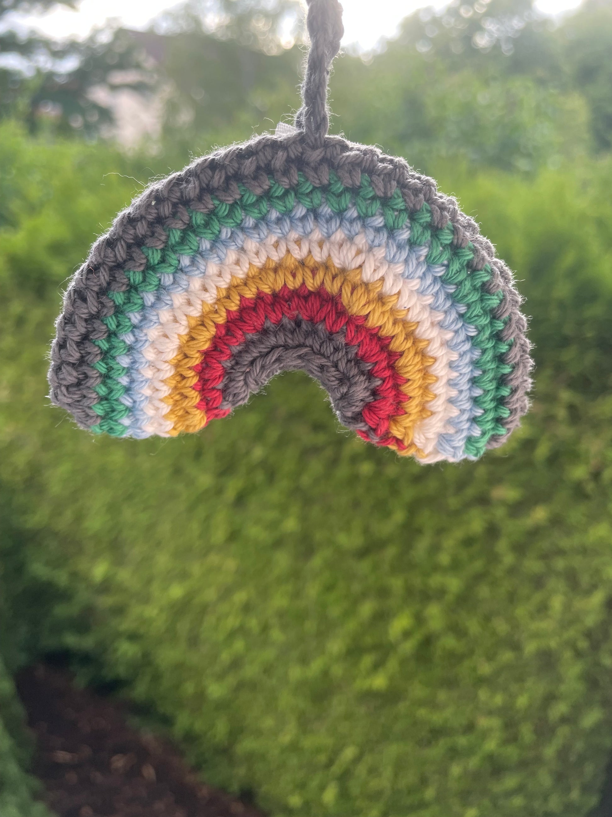 Gehäkelter Regenbogen Schlüsselanhänger mit Karabiner in den 6 Farben der Disability Pride Flagge: Grau, Grün, Blau, Weiß, Gelb, Rot. Außerdem hängt das Logo von Wirbelwind ebenfalls am Karabiner. Nähere Aufnahme.