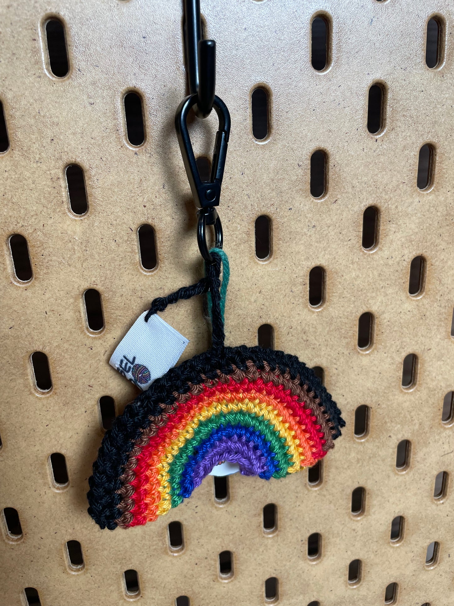 Gehäkelter Regenbogen Schlüsselanhänger mit Karabiner in den Farben der Philadelphia Pride Flagge: Schwarz, Braun, Rot, Orange, Gelb, Grün, Blau, Lila. Außerdem hängt das Logo von Wirbelwind ebenfalls am Karabiner.
