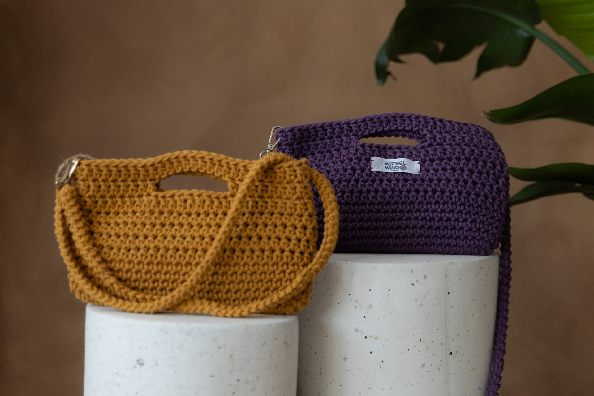 Nahaufnahme von Violeter und Gelber Tasche auf Betonsäulen. Gelb unscharf. Häkelmuster klar sichtbar.