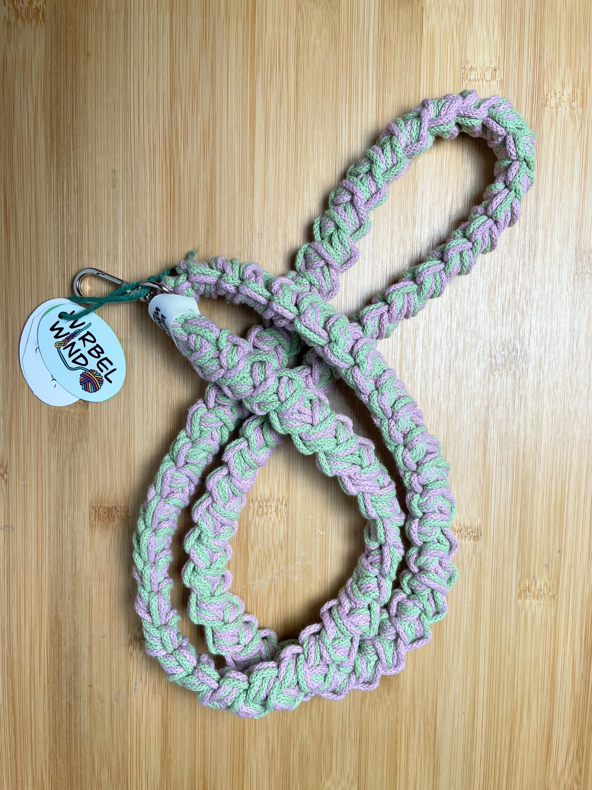 Rosa-Matchgrün-meliertes Lanyard kringelt sich. Wirbelwindlogo am unteren Ende, direkt über silbernem Karabiner angenäht.