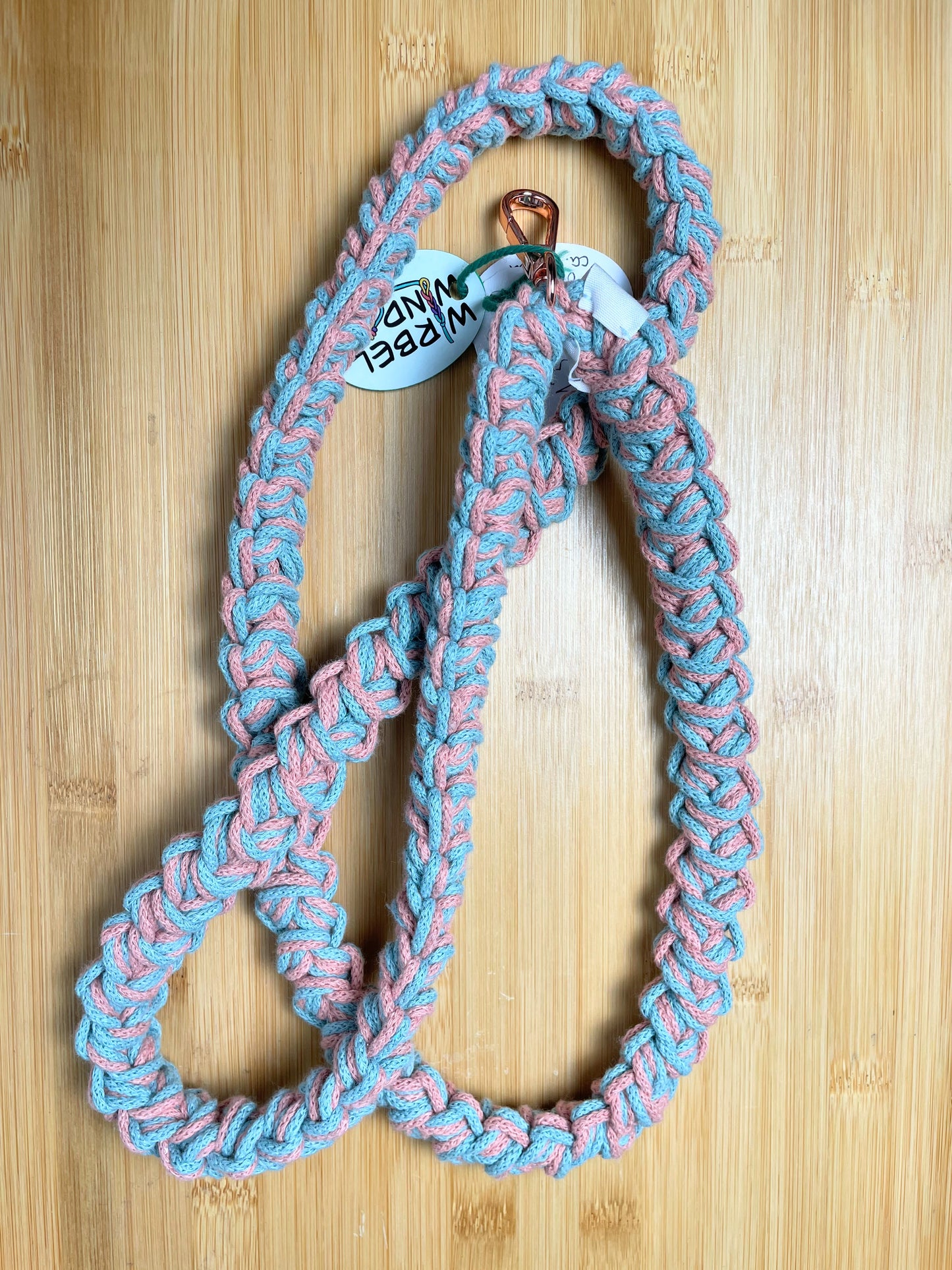 Rosa-Türkis-meliertes Lanyard kringelt sich. Wirbelwindlogo am unteren Ende, direkt über roségoldenem Karabiner angenäht.