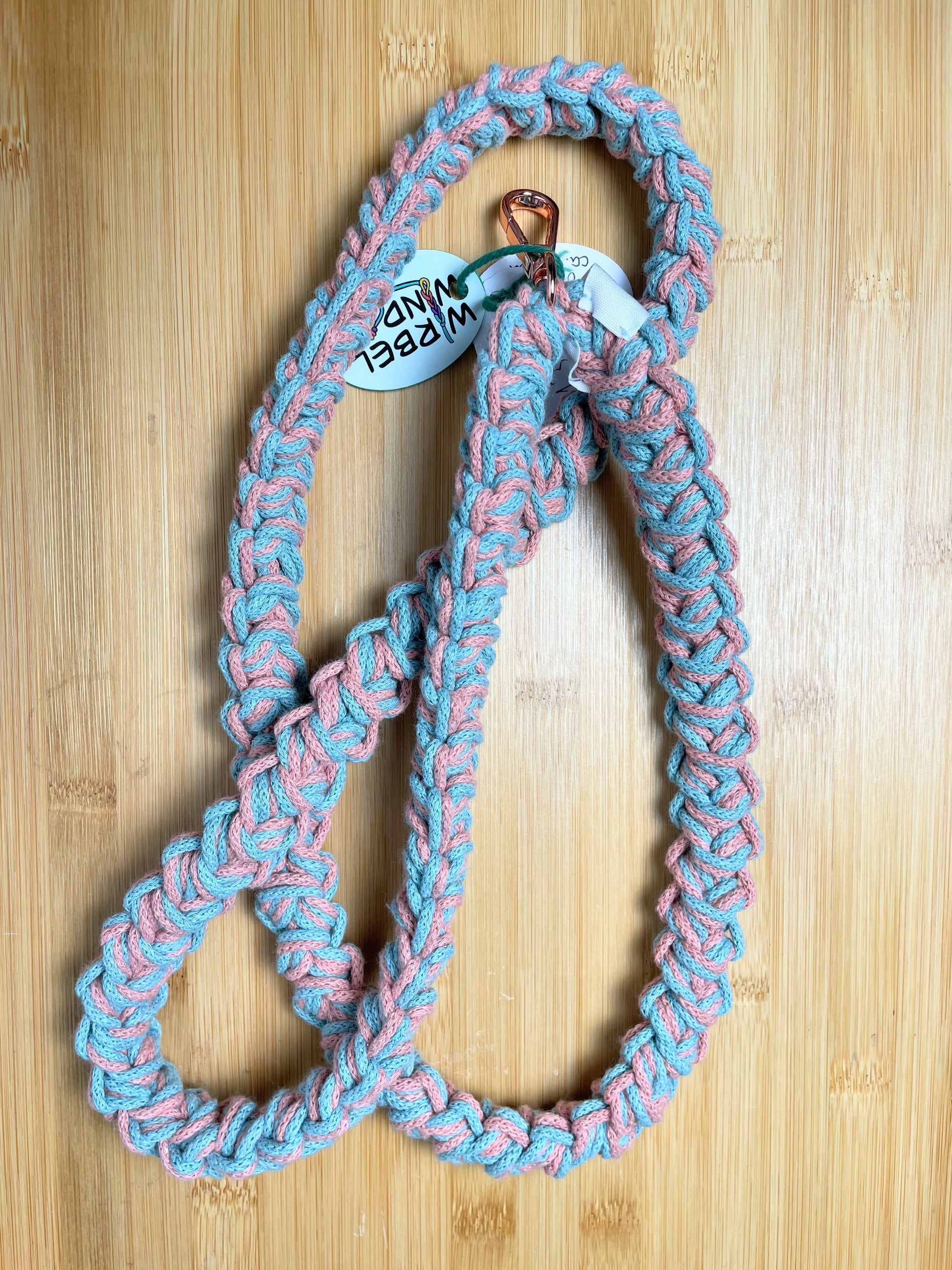 Rosa-Türkis-meliertes Lanyard kringelt sich. Wirbelwindlogo am unteren Ende, direkt über roségoldenem Karabiner angenäht.