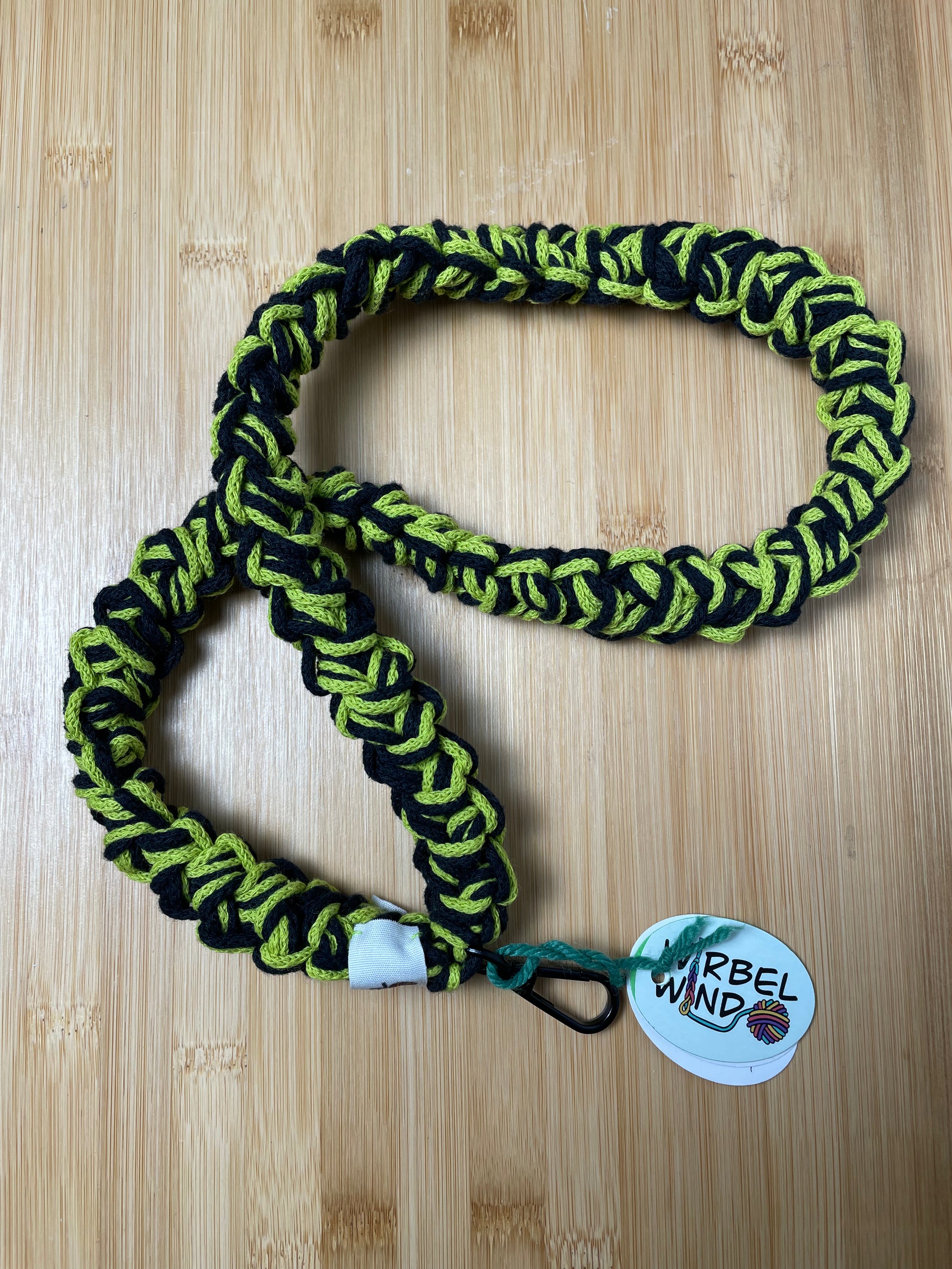 Schwarz-Rosa-Limegrün-meliertes Lanyard liegt verschlungen da. Wirbelwindlogo am unteren Ende, direkt über schwarzem Karabiner angenäht.