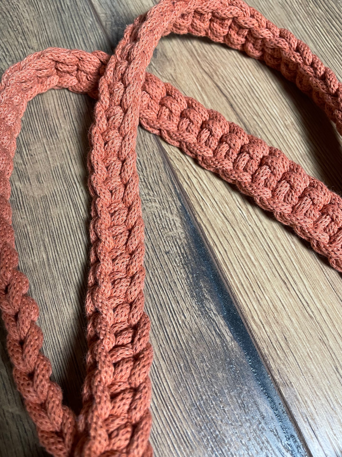 Detailansicht des Henkels der FLORA Schultertasche aus gehäkeltem recyceltem Baumwollgarn in Terracotta-Orange. Das Foto zeigt die Textur und das Muster der Häkelarbeit sowie die sorgfältige Verarbeitung der handgefertigten Tasche.