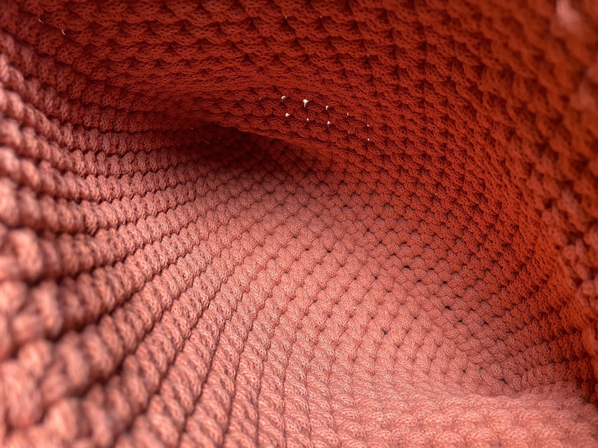 Detailansicht der FLORA Schultertasche aus gehäkeltem recyceltem Baumwollgarn in Terracotta-Orange. Das Foto zeigt das Innere der Tasche und daher die Textur und das Muster der Häkelarbeit sowie die sorgfältige Verarbeitung der handgefertigten Tasche.