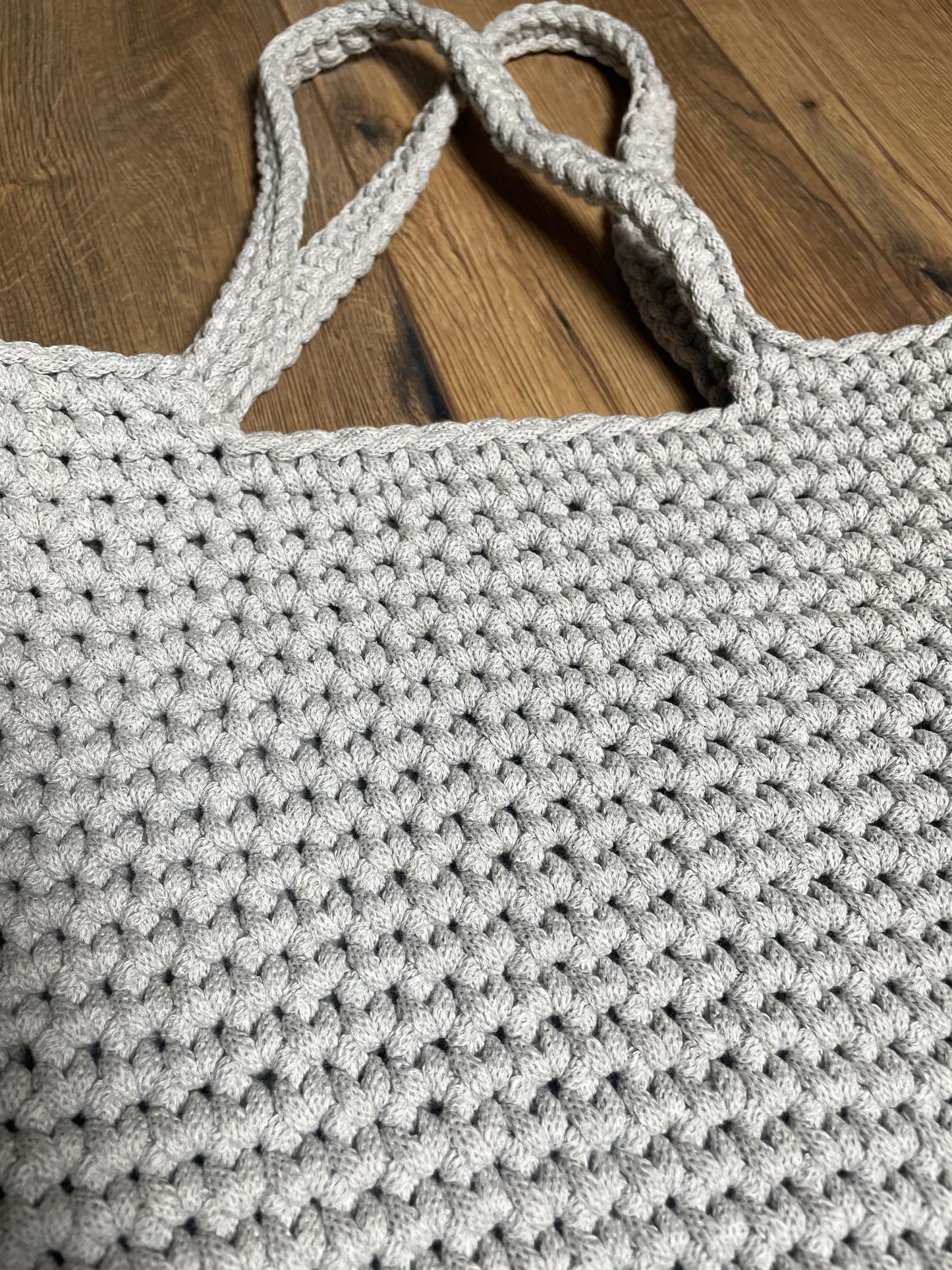 Nahaufnahme der FLORA Häkeltasche in hellgrauer Farbe. Das Bild zeigt deutlich die einzelnen Häkelmaschen und die Struktur des recycelten Baumwollgarns. Die handwerkliche Qualität und das gleichmäßige Maschenbild der Handarbeit sind gut erkennbar.