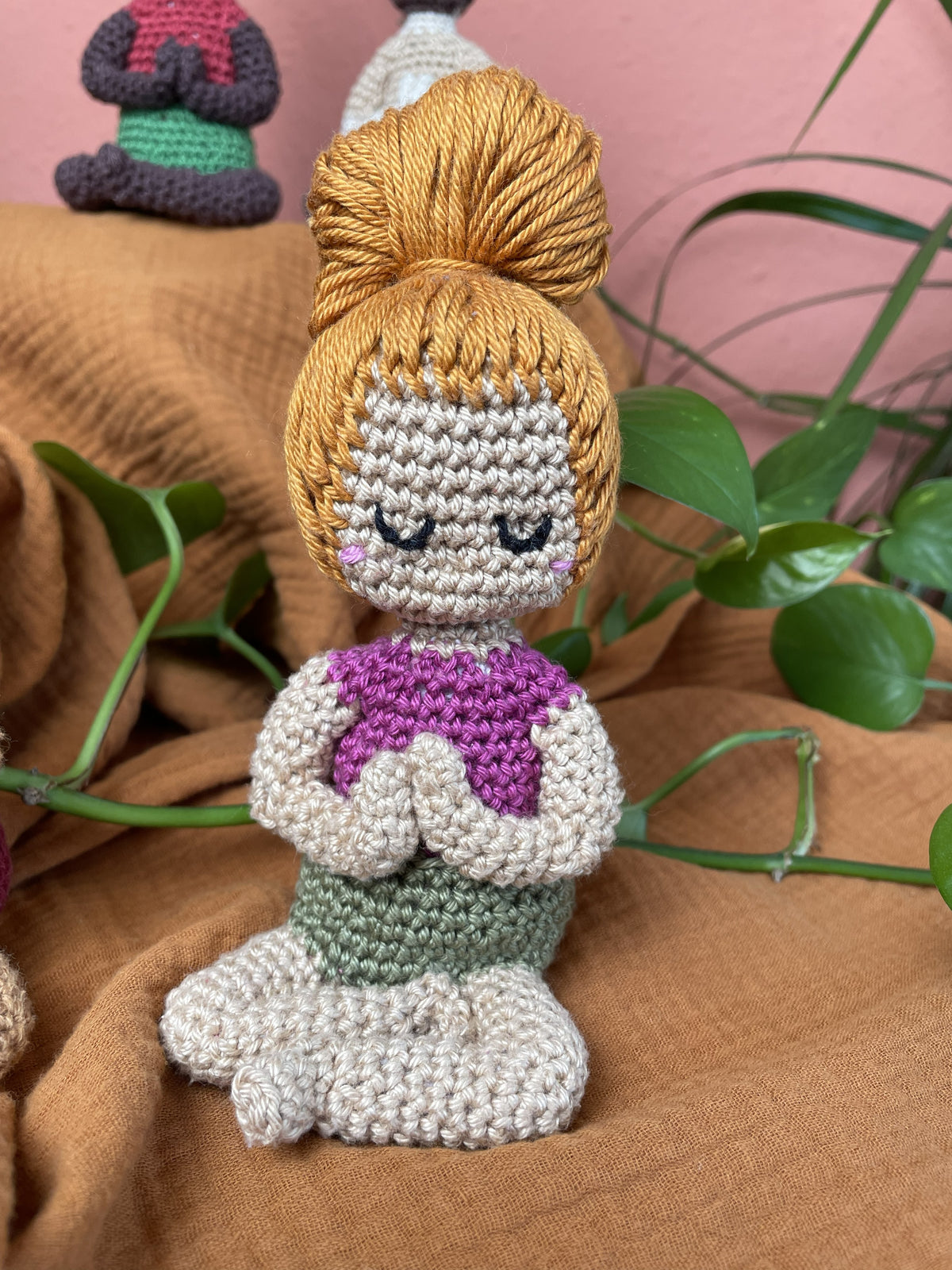 Weiblich aussehende Figur, dunkelbeige Hautfarbe, rot-oranges Haar zum Dutt gebunden,  olivgrüne kurze Hose, pinkes Shirt.