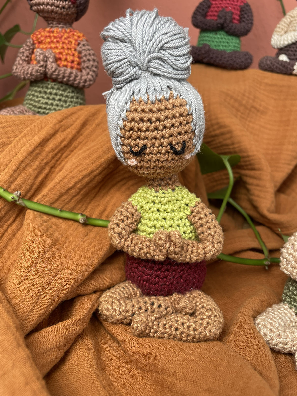 Weiblich-gelesene Figur, graues Haar zum Dutt gebunden, karamell-braune Haut, weinrote kurze Hose, apfelgrünes Shirt.