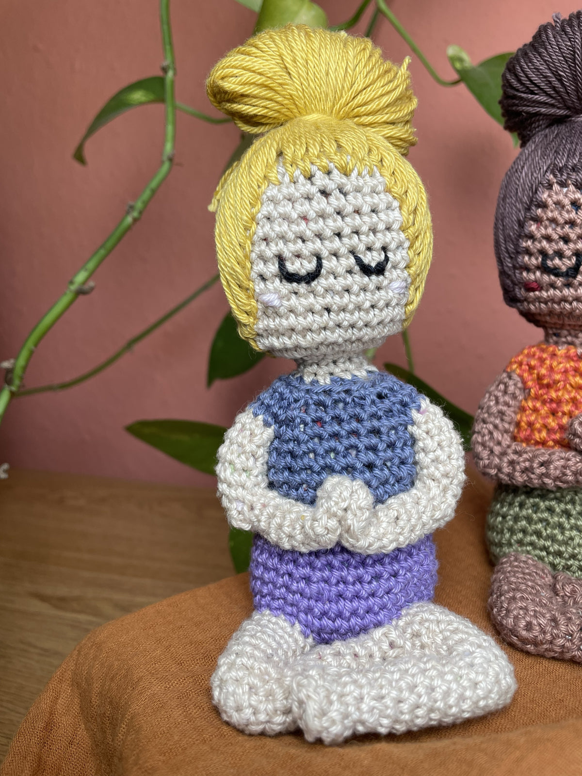 Weiblich-gelesene Figur, blondes Haar, hellbeige Hautfarbe, lila-farbene kurze Hose, blassblaues Shirt.