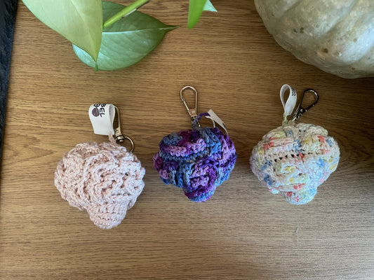 3 gehäkelte Gehirn-Schlüsselanhänger liegen nebeneinander (von links nach rechts): Rosa, Lila mit Farbverlauf, Weiß mit bunten Farbsprenklern.