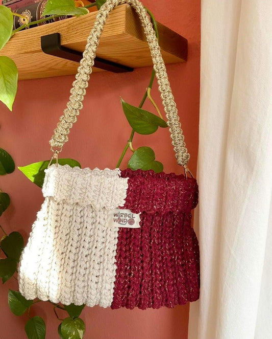 Tasche hängt am Henkel von Bücherregal, Efeutue im Hintergrund, wand Terrakotta, rechter Rand weißer Vorhang. Wir erkennen deutlich Häkelmuster und goldene Fäden im GArn.